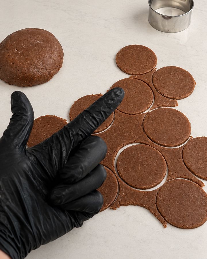 Chocolate cookie dough rolled out and cut into rounds, next to a round cutter