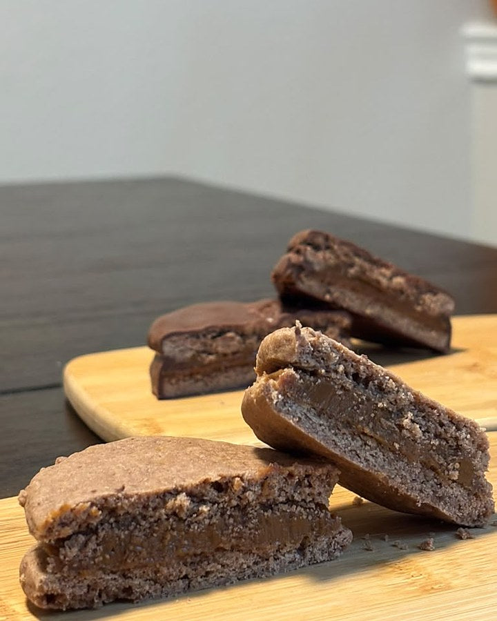 Chocolate alfajores cut open to show the thick dulce de leche filling, on a wooden board
